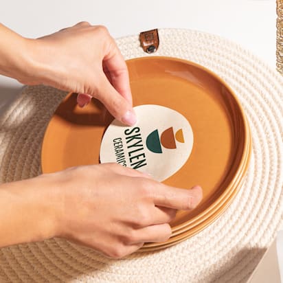 Hands applying a ceramic brand sticker to a red plate, showcasing logo design software in action.
