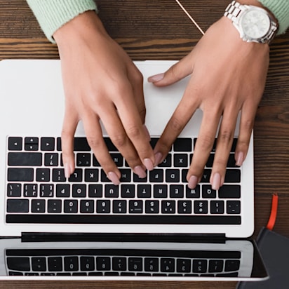 Hands typing on a laptop surrounded by stationery, coffee cup, and smartphone – web pages design software in use.