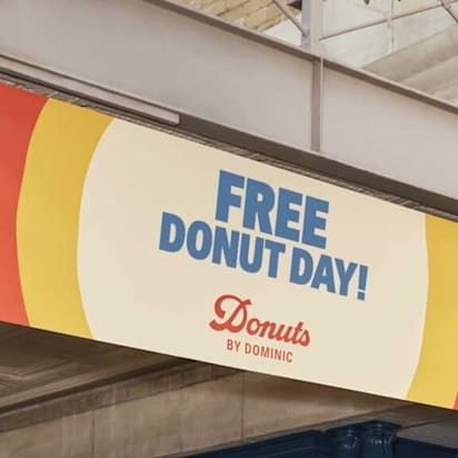 Donut company's overhead outdoor colourful (blue red and yellow borders) sign advertising "Free donut day!".