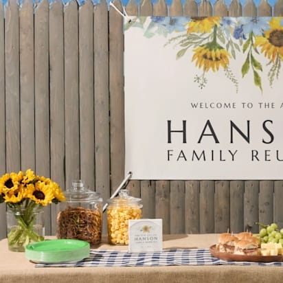 Outdoor event setup with a custom “Hanson Family Reunion” banner featuring sunflower illustrations, displayed above a snack and drink table.