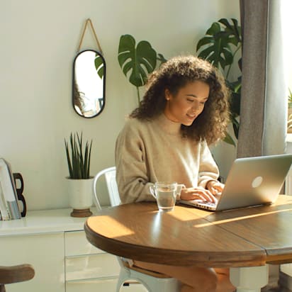 woman typing on a laptop next to a window surrounded by plants