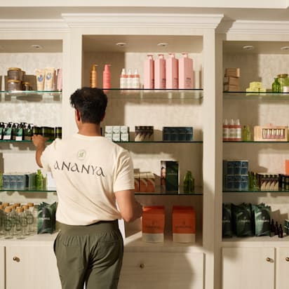 Staff member wearing a branded cream T-shirt while stocking shelves with matching retail products and packaging.