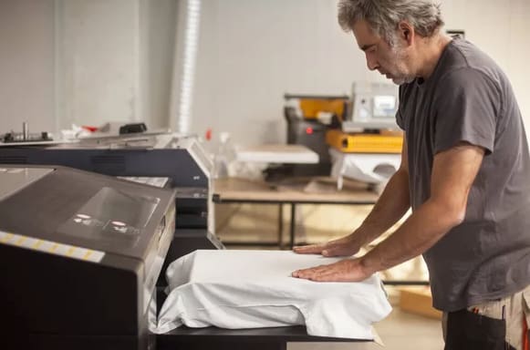 Professional graphic print technician works on digital t-shirt printing machine printer in professional printing shop