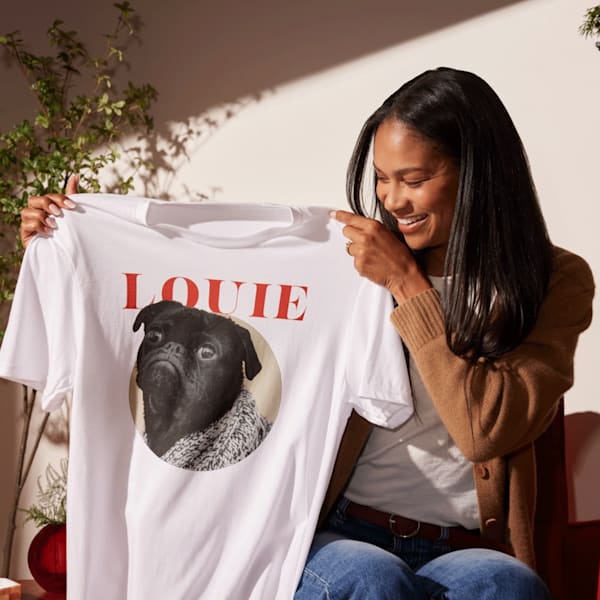Woman holding a white T-shirt with a printed photo of a pug dog and the name Louie.