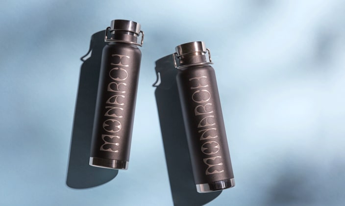 Two sleek, matte black metal water bottles with glossy branding laying on a teal background.