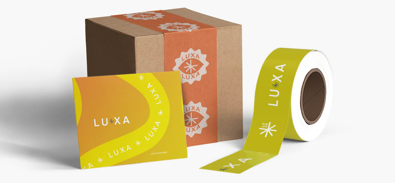 A simple brown cardboard cube mailer box with branded tape over it, a roll of branded tape and a yellow insert with matching branding.