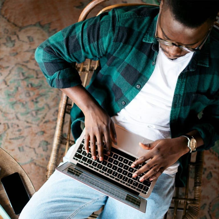Man working on a laptop, the perspective is from top down so the keyboard, not the screen, is in view.