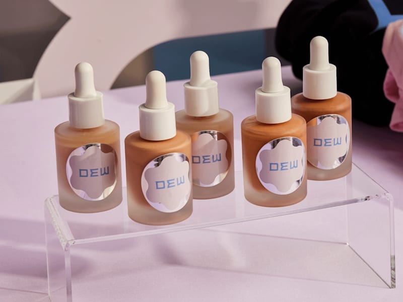 Five cosmetic dropper bottles with custom printed product labels displayed on a clear acrylic stand