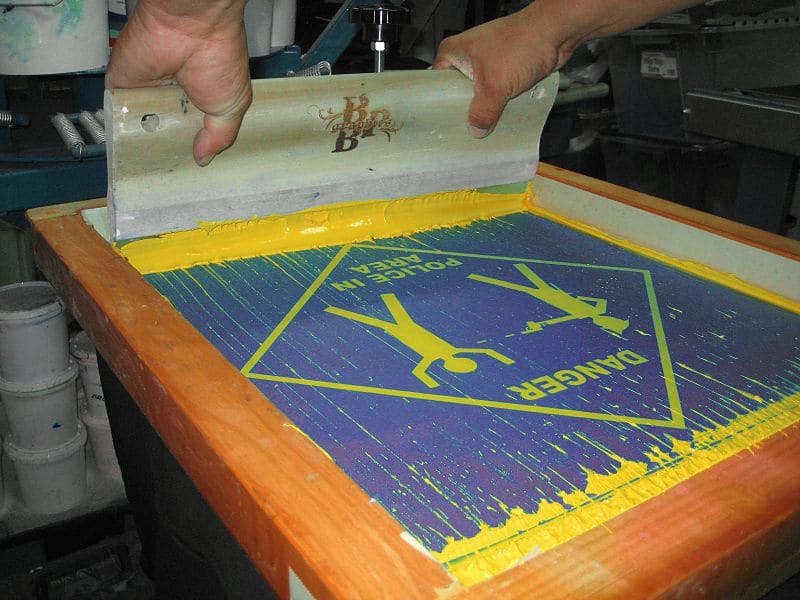 Close-up of a person’s hands pushing ink with a squeegee on a screen printer