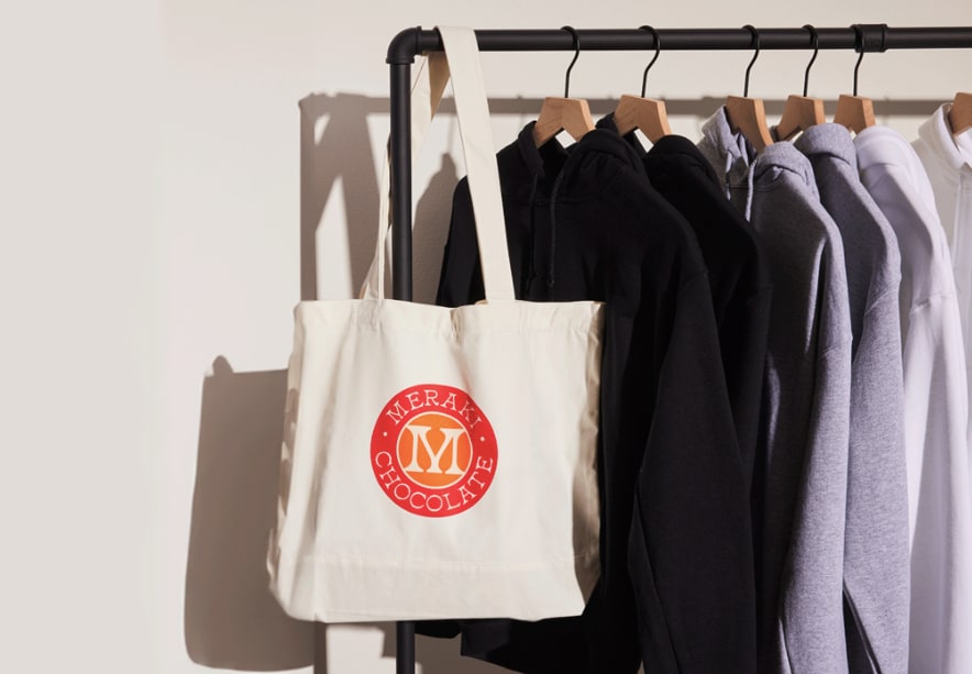 Tote bag with red logo hanging on a rail with hoodies