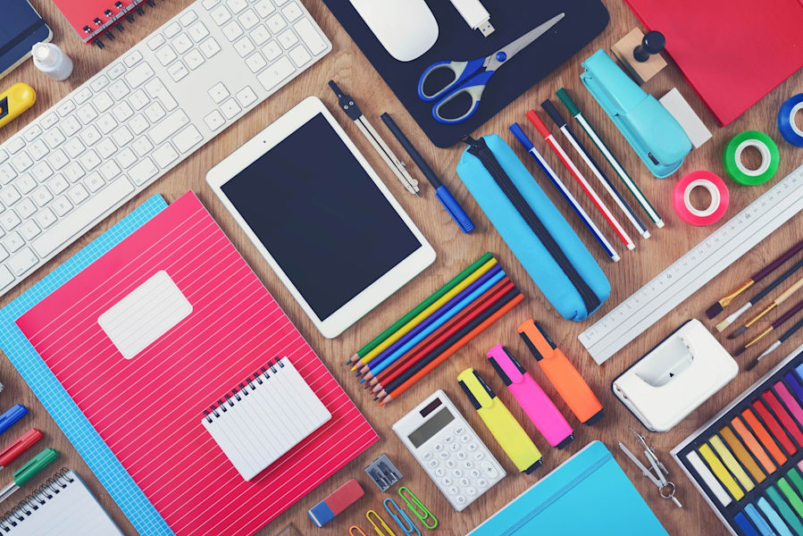 Flat lay of colorful notebooks, pencils, markers, and digital tools on a desk, representing personalized school supplies.