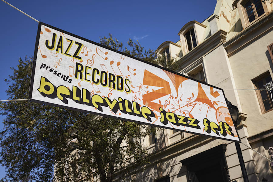 Example of a banner hanging across a roadway announcing the city’s jazz festival, features playful yellow font with black drop shadow