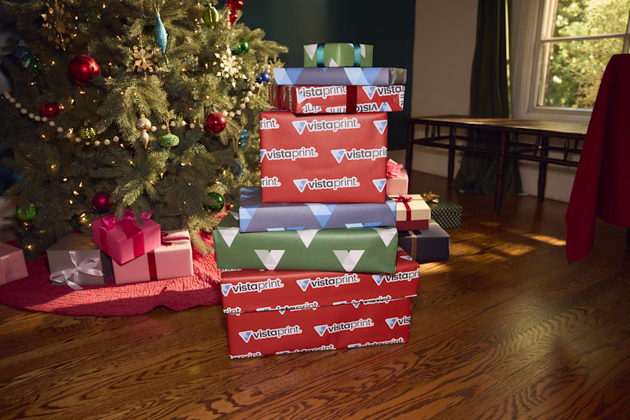 Paquets cadeaux empilés avec un emballage VistaPrint sous un sapin de Noël – parfait exemple de branding festif pour les conseils marketing de fin d’année des petites entreprises.