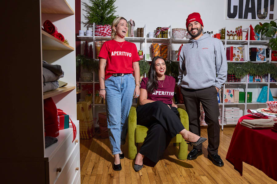 Business holiday prep example: three smiling people wearing branded Aperitivo accessories, t-shirts, and promotional materials in the background.