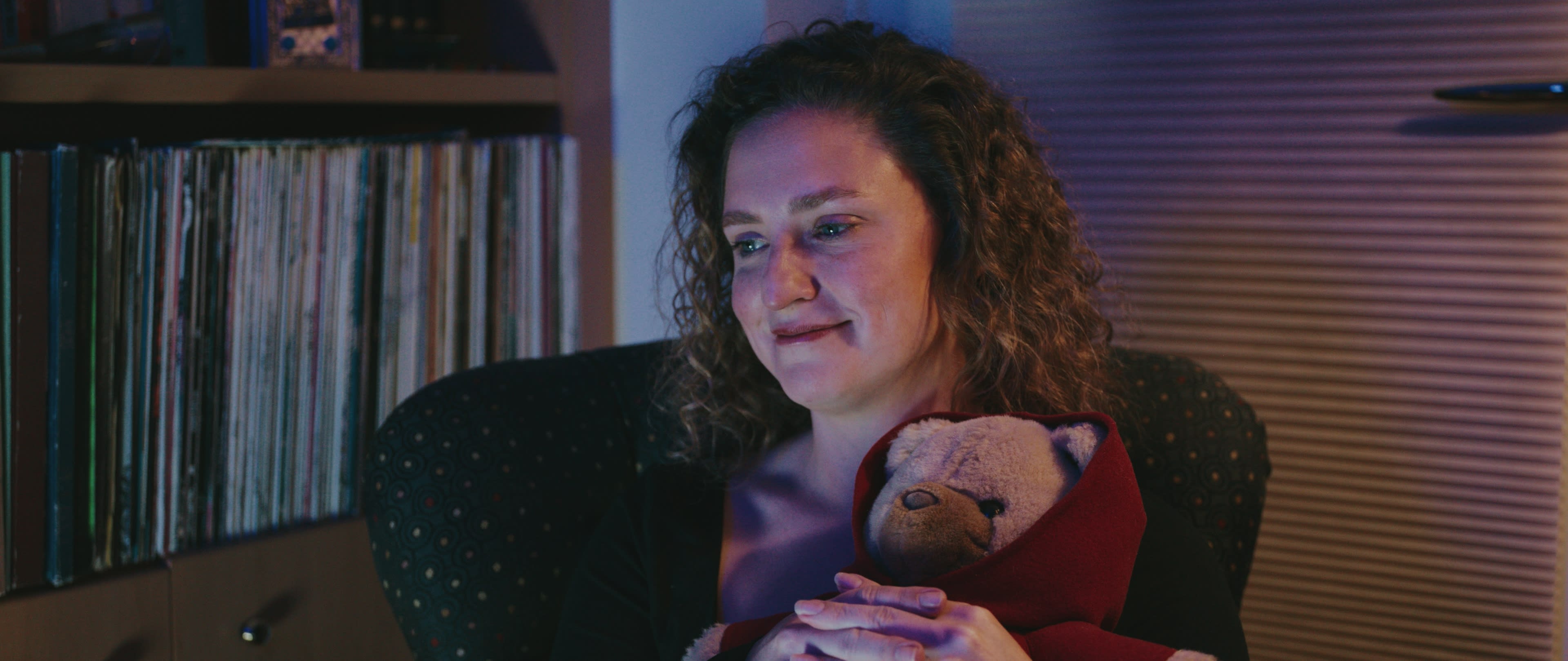 Hannah holds a childhood bear while watching family archive footage