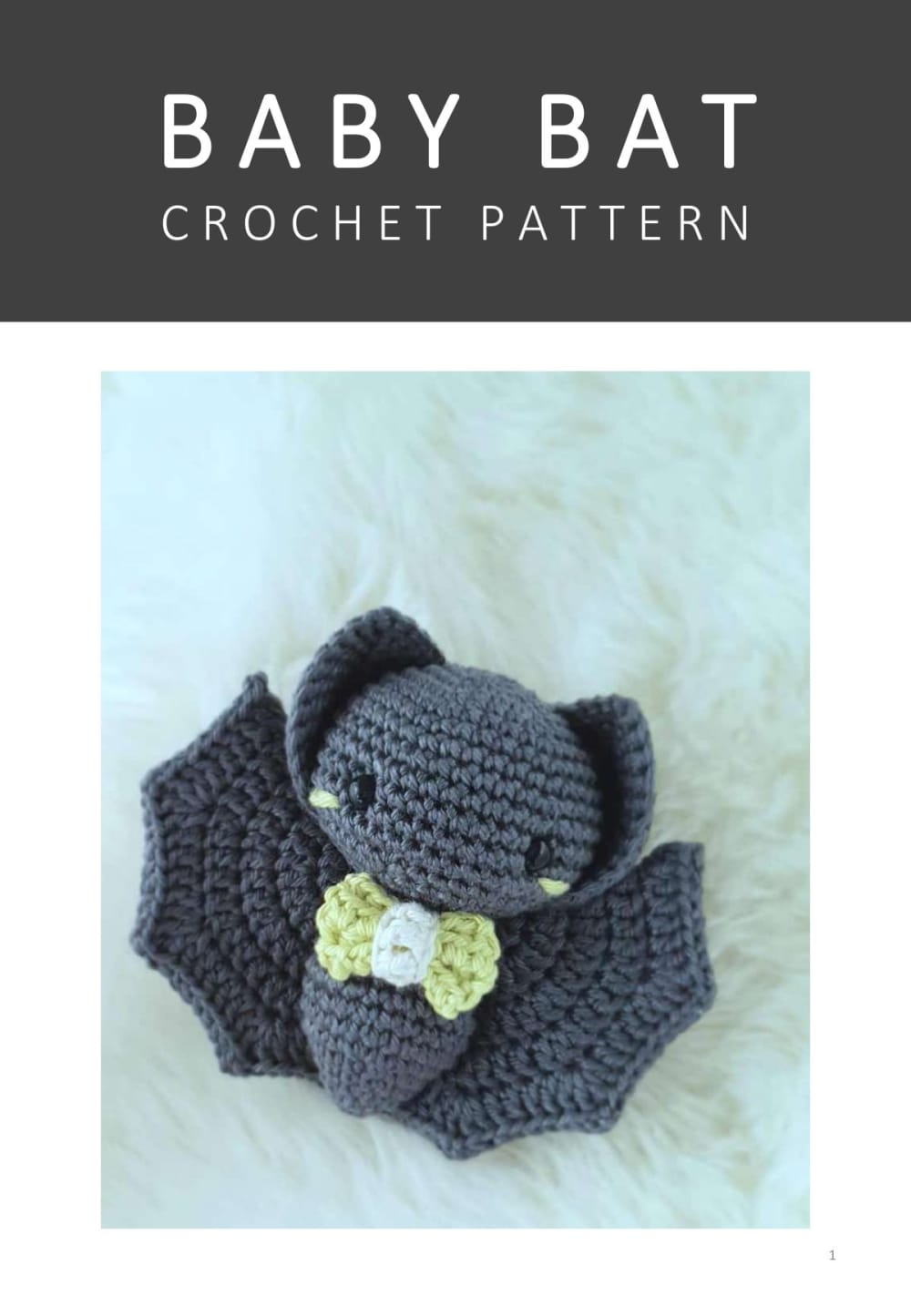 Dark grey crochet baby bat with a lime green bow tie sitting on a white fur rug