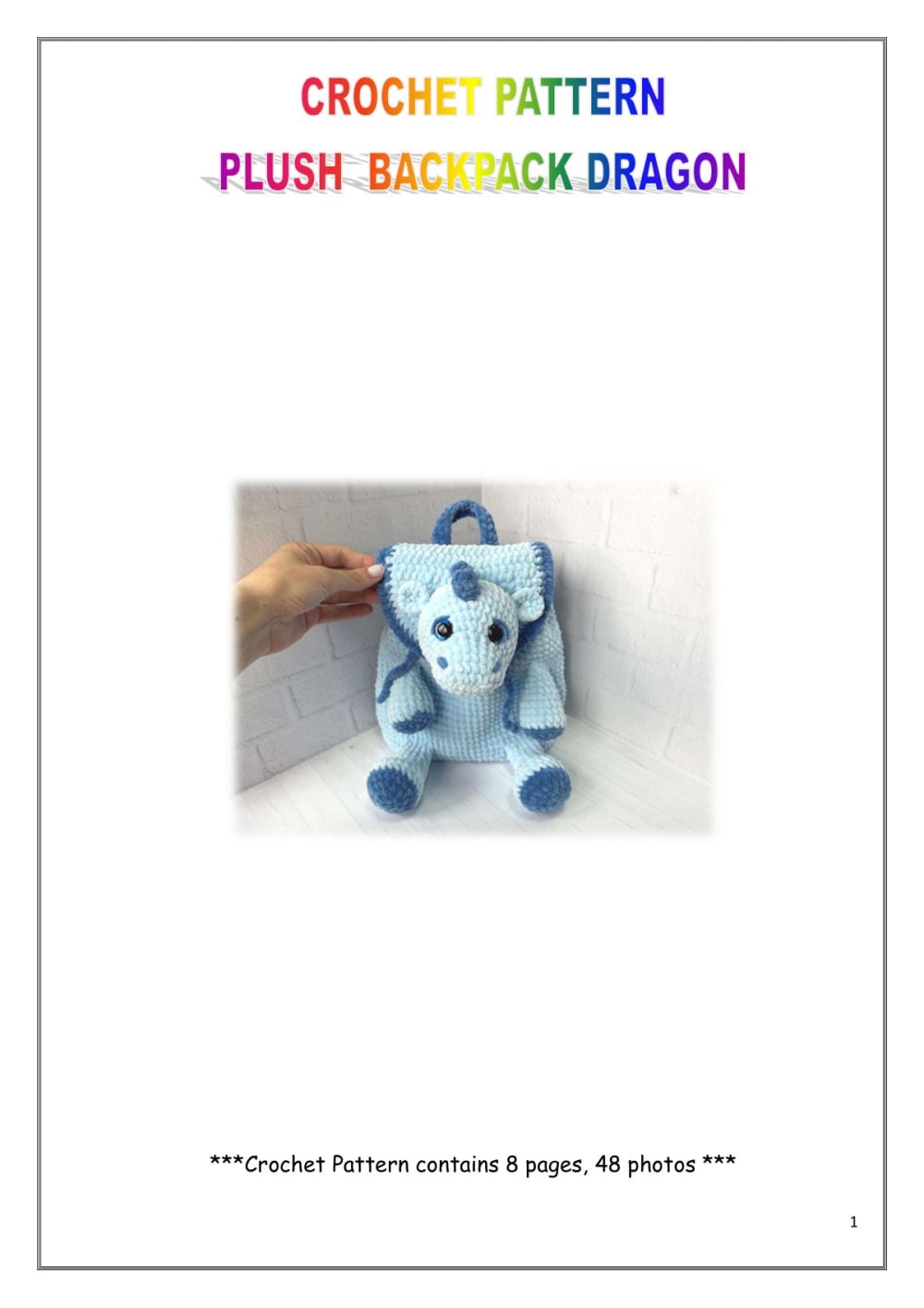 Hand holding a small light blue plush crochet dragon backpack with a dark blue trim