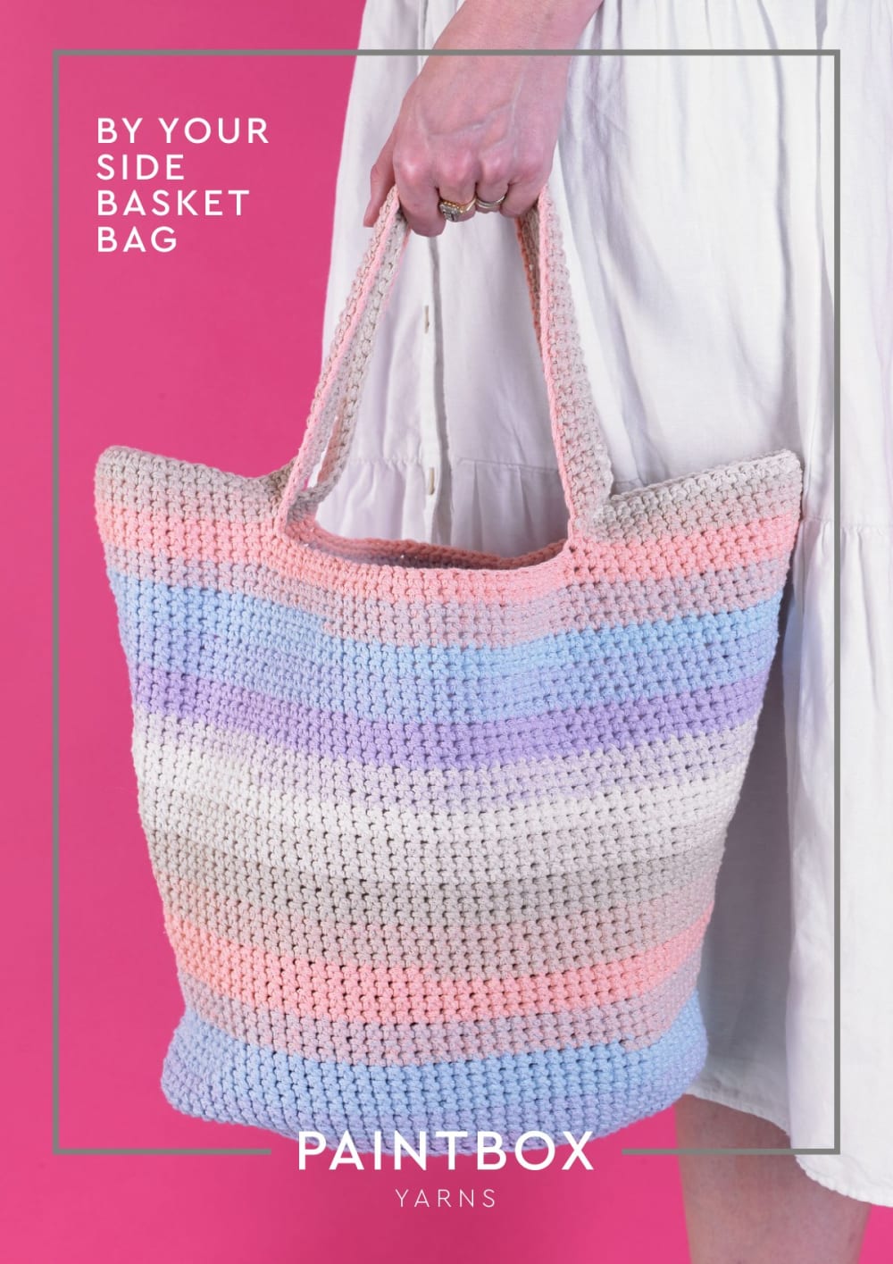 Woman holding a striped pastel pink, blue and cream crochet basket bag against a pink background