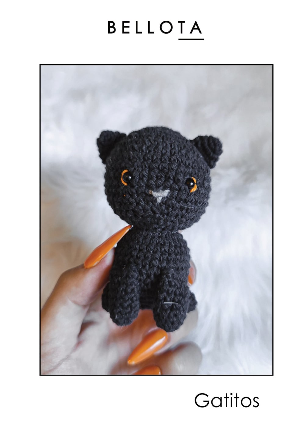 Small black crochet kitten with orange eyes sitting on a white furry blanket