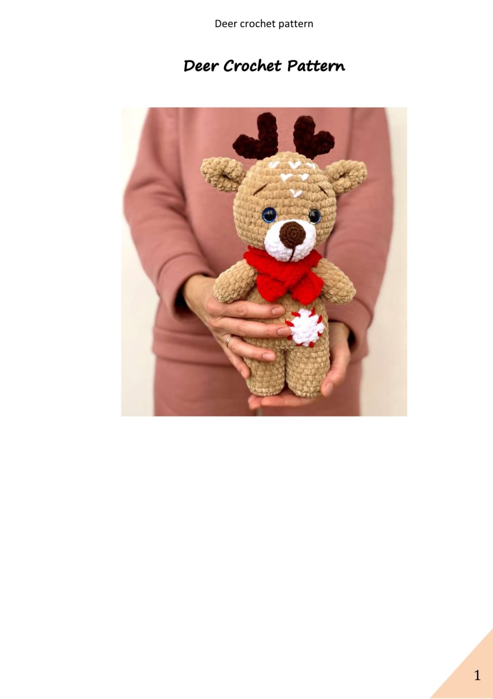 Woman holding a light brown plush crochet deer with dark antlers, a red scarf and a snowflake patch