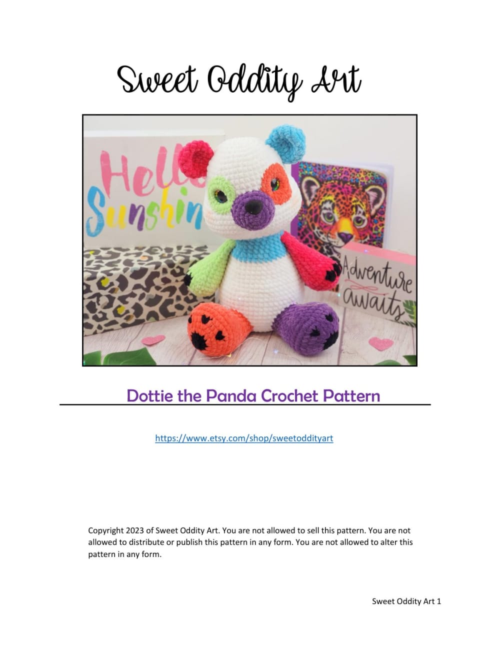 White crochet panda with colorful rainbow patches next to a bright Hello Summer sign