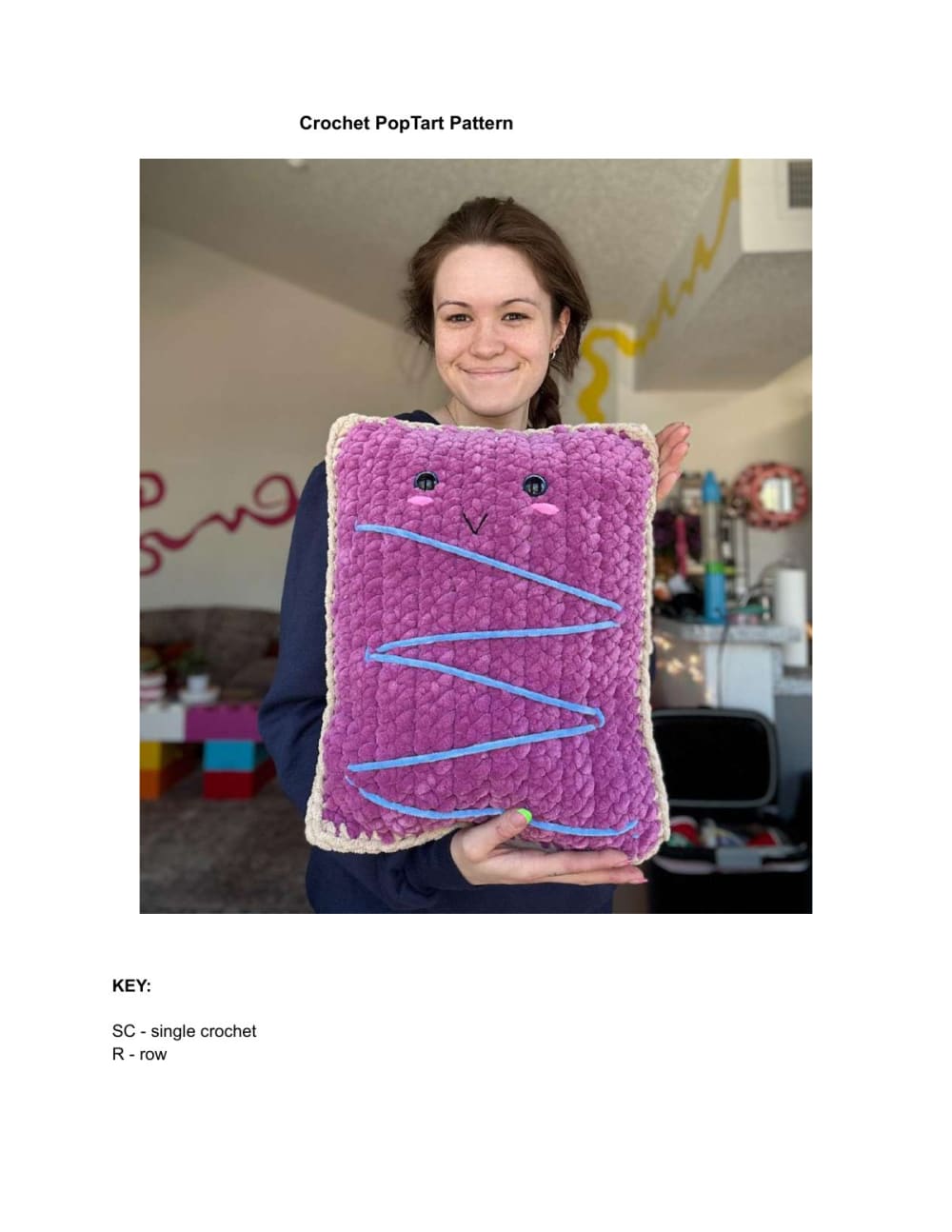 Woman holding a large crochet toaster pastry pillow with pink frosting and blue sprinkles