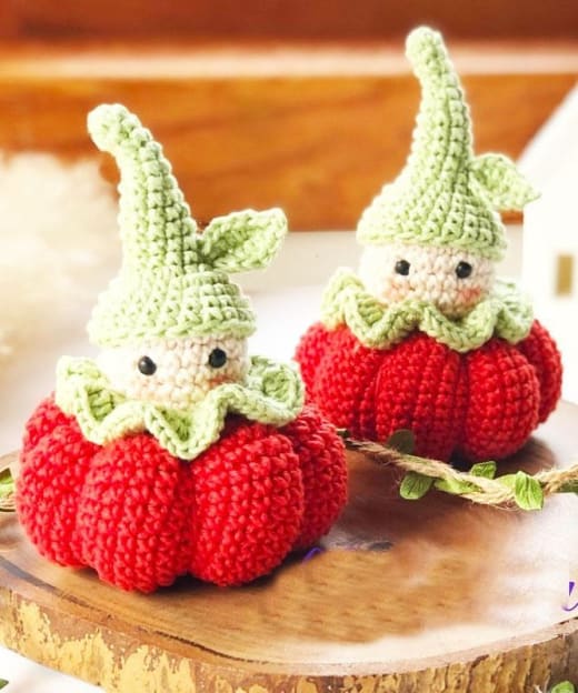 Crochet gnome pattern: two amigurumi gnomes in red crochet pumpkins with pointed light green hats on a wooden slice