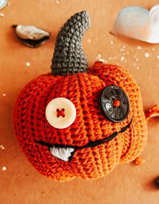 Button eye pumpkin crochet pattern: orange amigurumi pumpkin with a large white button eye, a dark button eye and a gray stem
