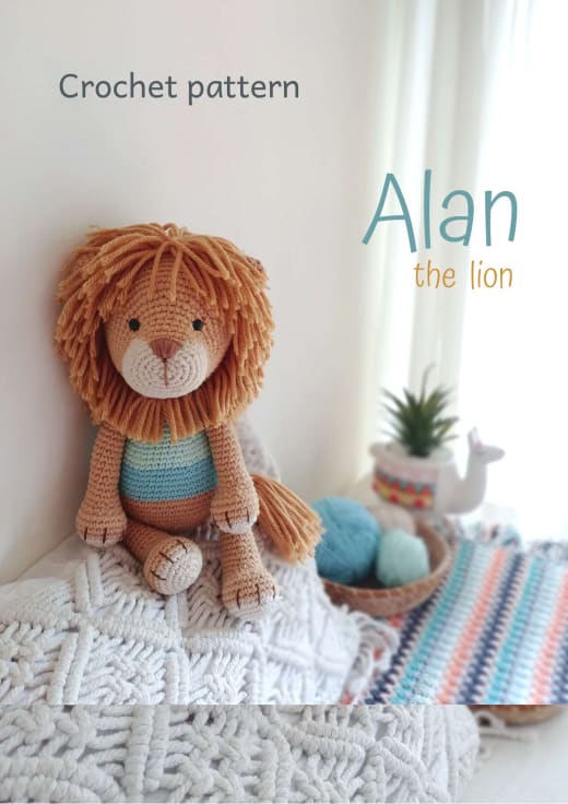 Amigurumi lion with a camel mane and a turquoise striped T-shirt sitting on a knitted blanket