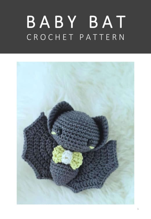Dark grey crochet baby bat with a lime green bow tie sitting on a white fur rug