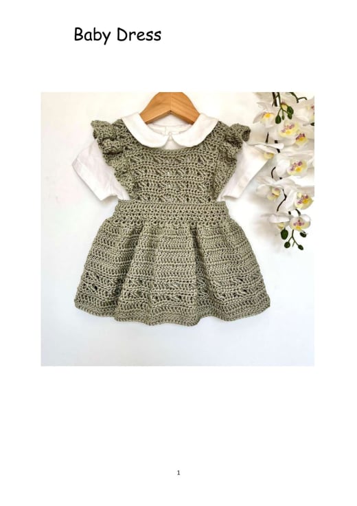 Olive green crochet baby pinafore dress with ruffle straps worn over a white blouse