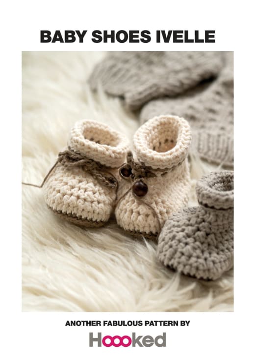 Cream crochet baby shoes with a folded cuff and a small button, placed on a white fur rug