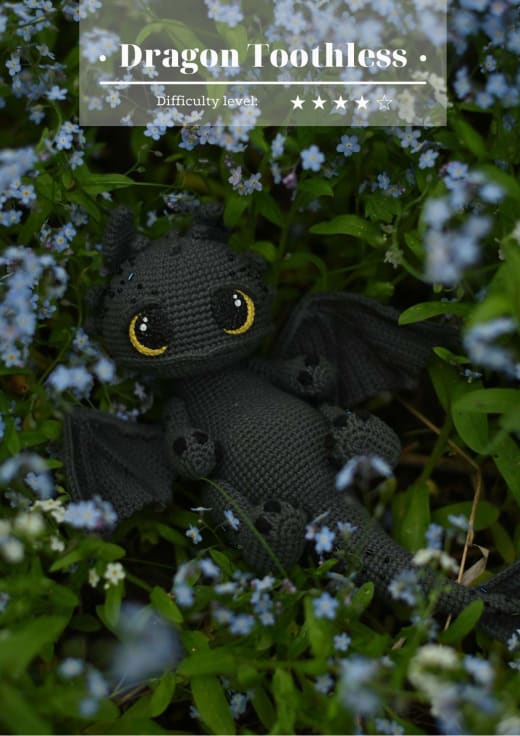 Black crochet dragon with big yellow eyes sitting among blue flowers