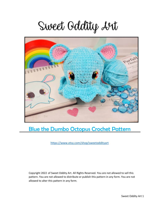 Turquoise Dumbo octopus crochet toy with big eyes, pink ears and a frill next to a rainbow drawing