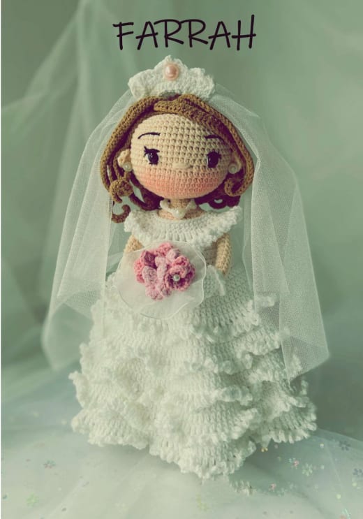 Crochet bride doll with long wavy hair, a tulle veil and a tiered white ruffle wedding dress holding a pink bouquet