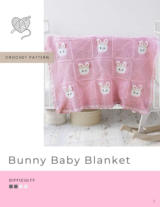 Pink crochet baby blanket with white bunny faces on granny squares, laid over a crib