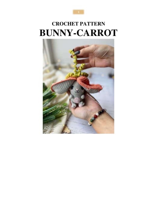 Small gray crochet bunny peeking out of an orange carrot with green leaves held in a hand