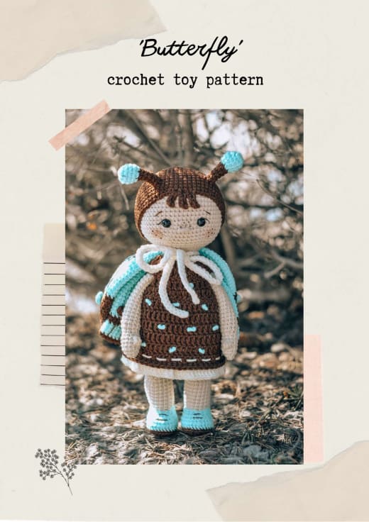 Amigurumi butterfly doll with a brown cap and antennae, a chocolate dress and turquoise wings standing outdoors