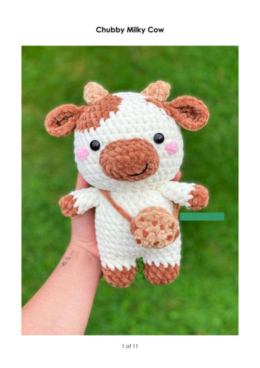 Chubby white and brown crochet cow with rosy cheeks and a small cookie bag held in a hand