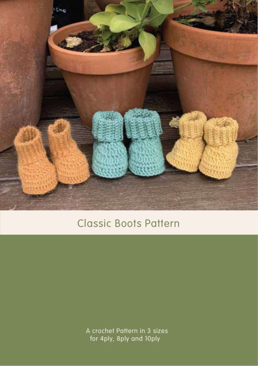 Three pairs of crochet baby boots with ribbed cuffs in orange, turquoise and yellow standing among plant pots