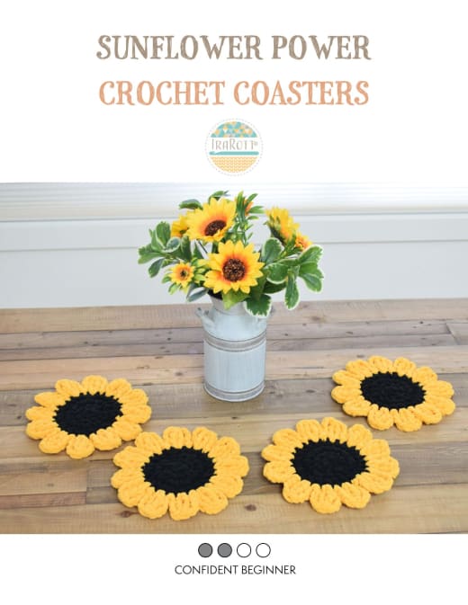 Four black and yellow crochet sunflower coasters on a wooden table next to a vase of sunflowers