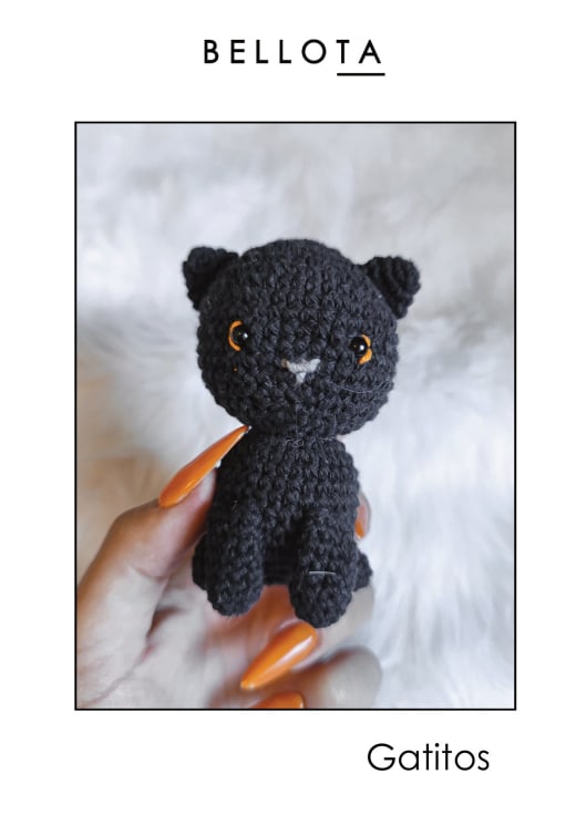 Small black crochet kitten with orange eyes sitting on a white furry blanket