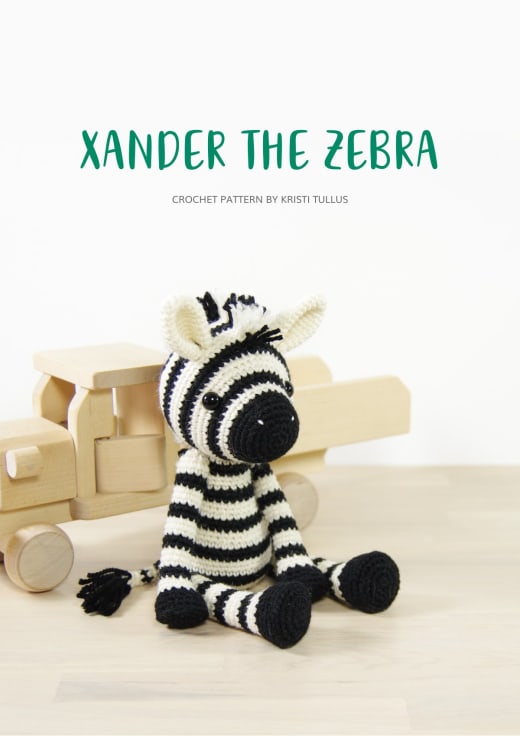 Black and white striped crochet zebra sitting on a wooden toy
