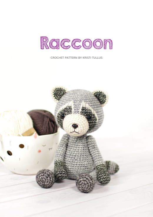 Grey crochet raccoon with a dark eye mask and a striped tail