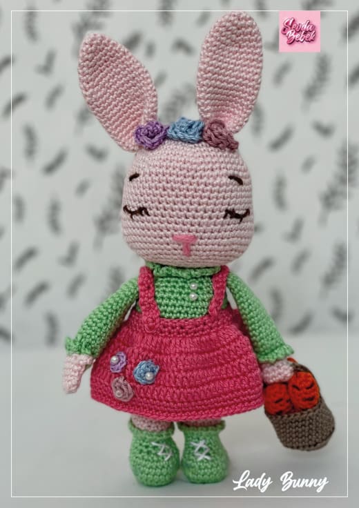 Pink crochet bunny in a dark pink dress and green top with flowers on her ears