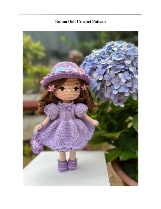 Emma doll in a light purple dress and hat with hydrangeas behind