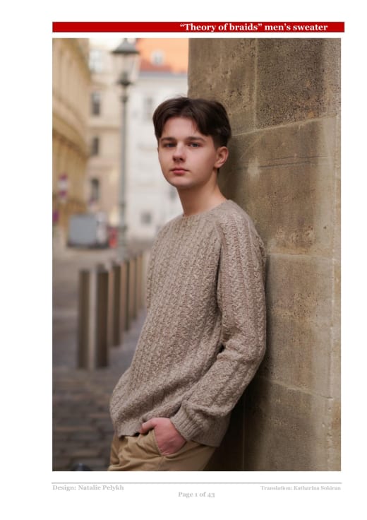 Man wearing a beige cable knit sweater leaning on a wall