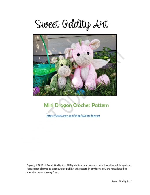 Green crochet dragon with a cream belly and pink wings sitting