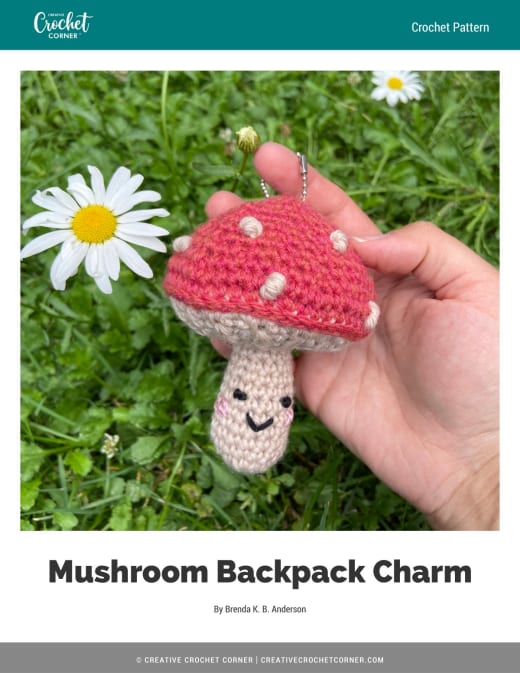 Red and white crochet mushroom charm with a smile held in a hand