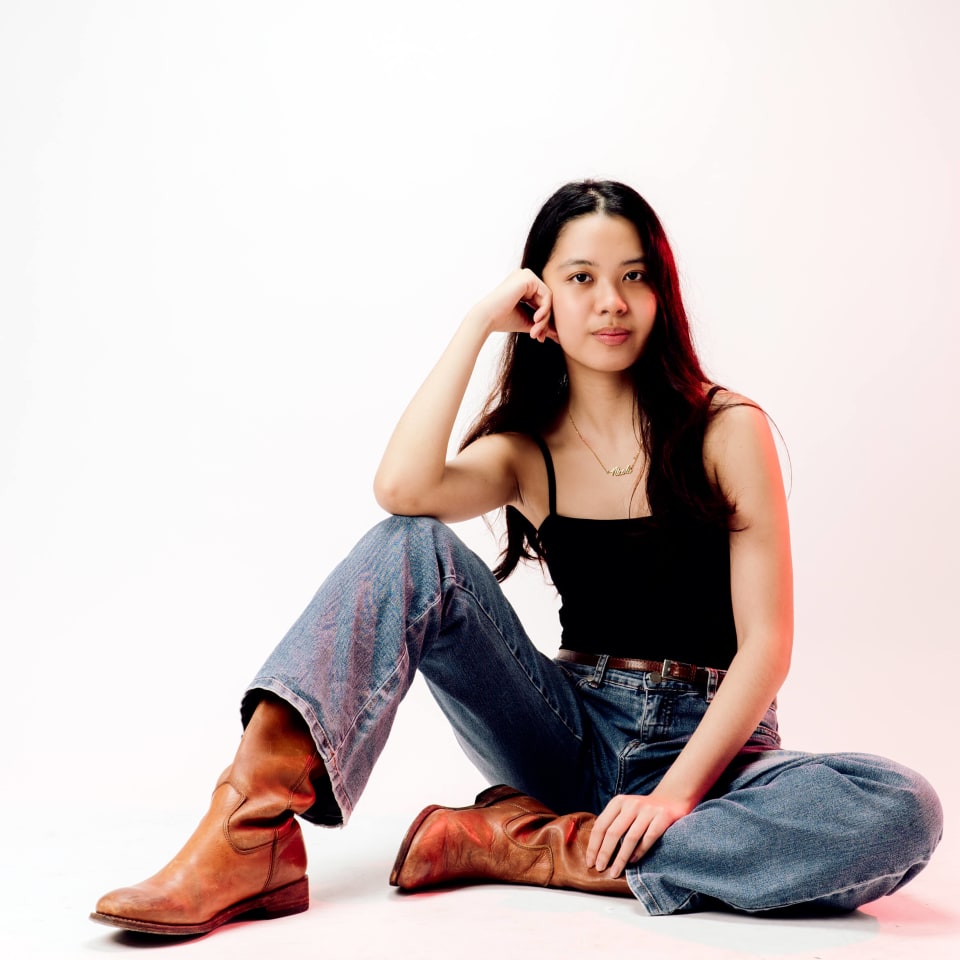 Seated portrait on the floor, head tilted, pink backdrop